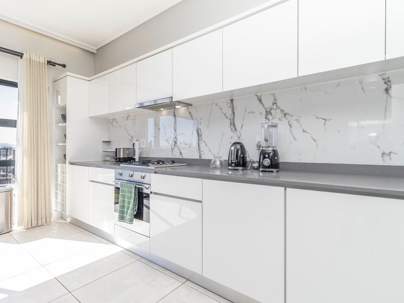 Modern kitchen featuring white gloss cabinetry, marble-look splashback, stone countertops, and integrated appliances, with direct access to a balcony.