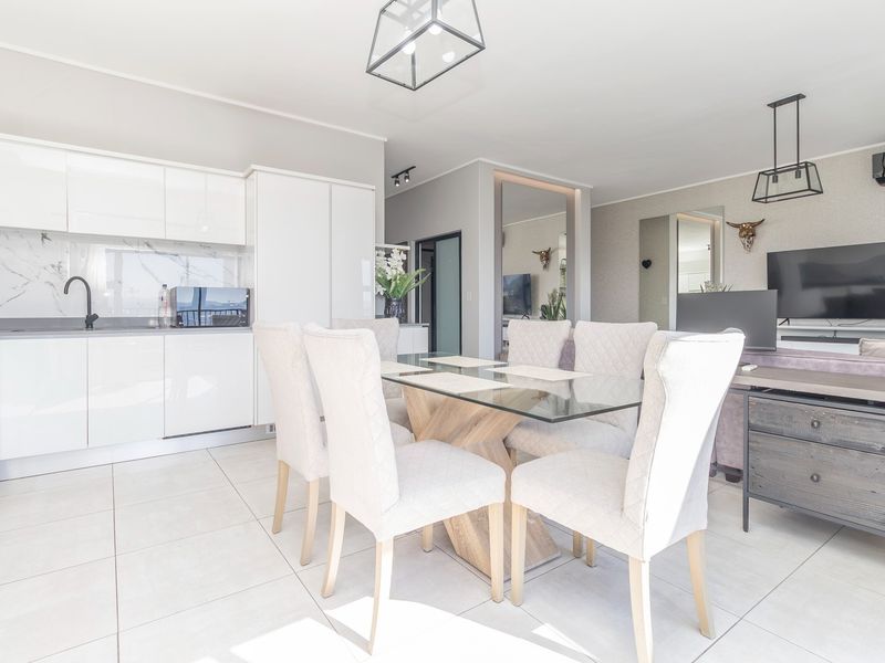 Modern open-plan living and dining area featuring sleek white kitchen cabinetry, marble-look splashback, tiled floors, and contemporary pendant lighting.