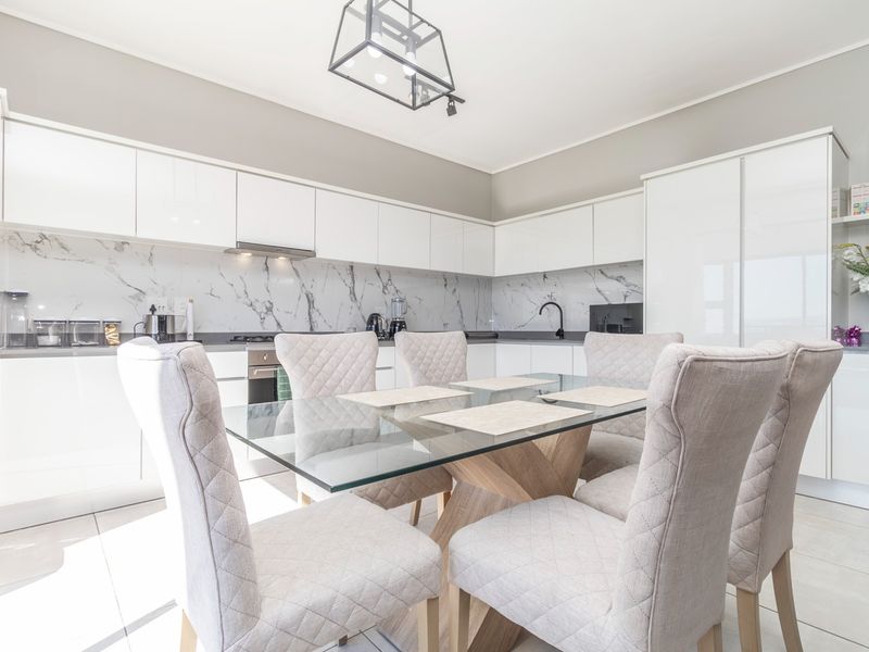 Modern open-plan kitchen featuring high-gloss white cabinetry, marble-look splashbacks, integrated appliances, and sleek finishes, seamlessly flowing into the dining area.