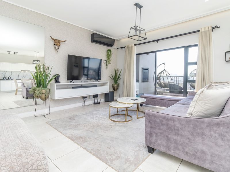 Modern open-plan living area featuring tiled floors, air conditioning, and large sliding glass doors leading to a balcony, with an integrated kitchen visible.