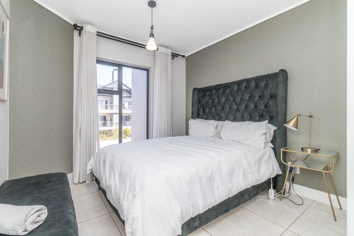 A well-maintained bedroom featuring tiled flooring, neutral textured wallpaper, and a sliding glass door providing natural light and access to the exterior.