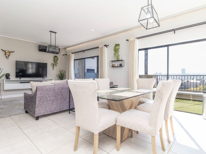 Bright open-plan living and dining area featuring tiled floors, modern pendant lighting, and large sliding glass doors leading to a balcony with city views.