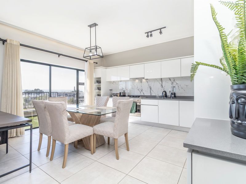 Modern open-plan kitchen and dining area featuring sleek white cabinetry, marble-look splashback, integrated appliances, and large sliding doors leading to a balcony.