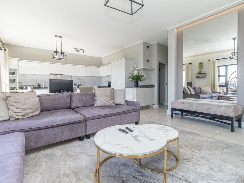 Modern open-plan living area featuring a sleek kitchen with marble-look backsplash, integrated cabinetry, and bright, contemporary finishes throughout the space.