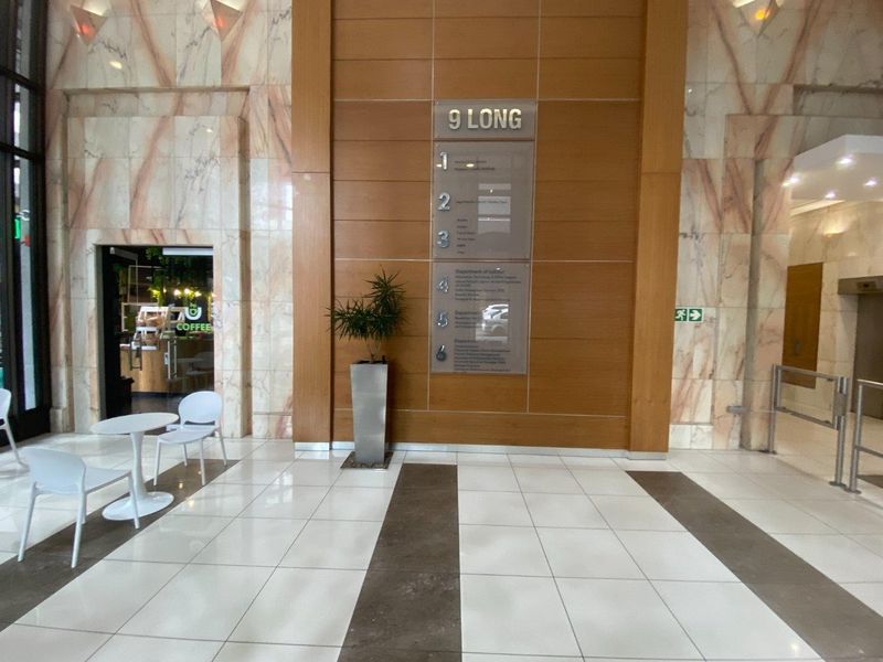 Modern commercial building lobby featuring marble wall accents, wood paneling, and a clear directory signage board for multiple office levels.