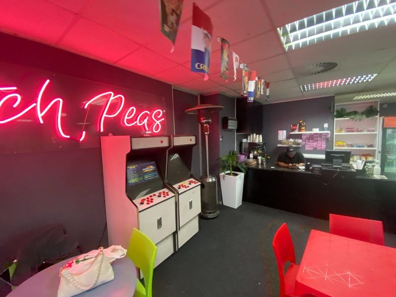 Commercial open-plan space featuring a service counter, suspended ceiling with recessed lighting, and neon wall signage, suitable for a cafe or entertainment venue.