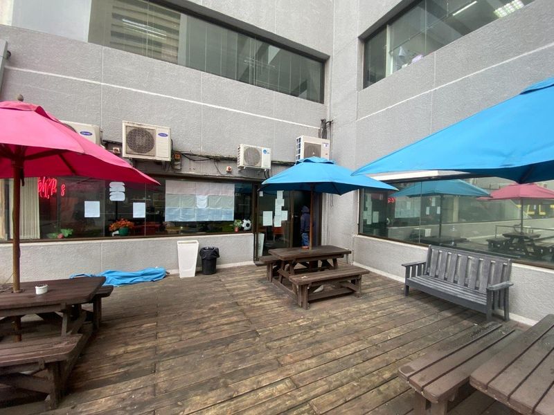 Outdoor commercial patio area featuring timber decking, wall-mounted air conditioning units, and large glass windows providing access to the interior space.