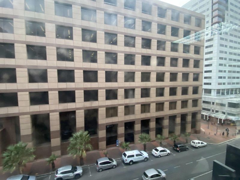 A street-level view of a multi-story commercial office building featuring a grid-patterned facade with tinted windows and an adjacent paved sidewalk.