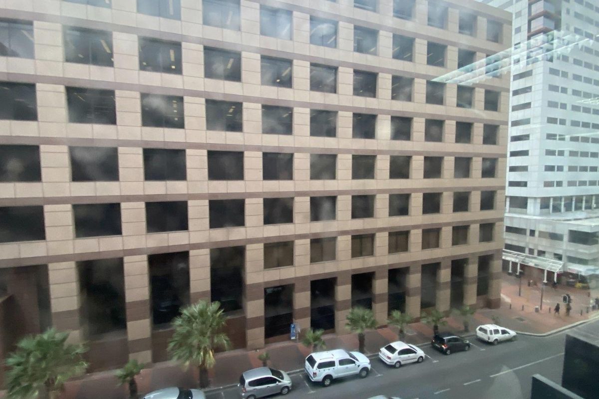 A street-level view of a multi-story commercial office building featuring a grid-patterned facade with tinted windows and an adjacent paved sidewalk.