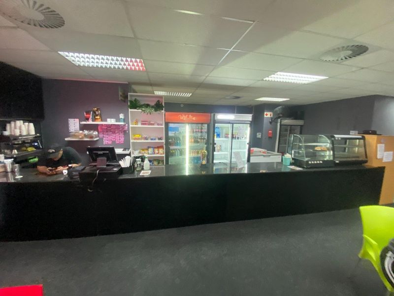 Commercial service counter area featuring a long black granite countertop, integrated display refrigeration units, and functional suspended ceiling lighting.