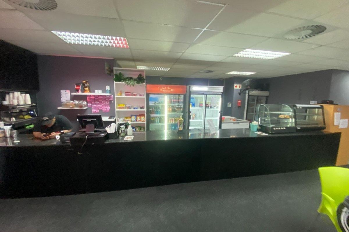 Commercial service counter area featuring a long black granite countertop, integrated display refrigeration units, and functional suspended ceiling lighting.