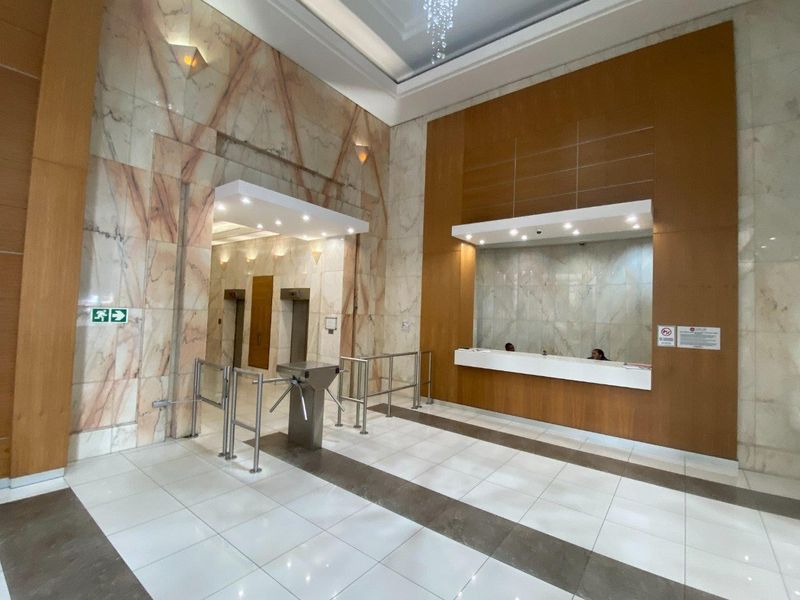 Modern commercial building lobby featuring marble wall finishes, a dedicated reception desk, secure turnstile access, and elevator bank.