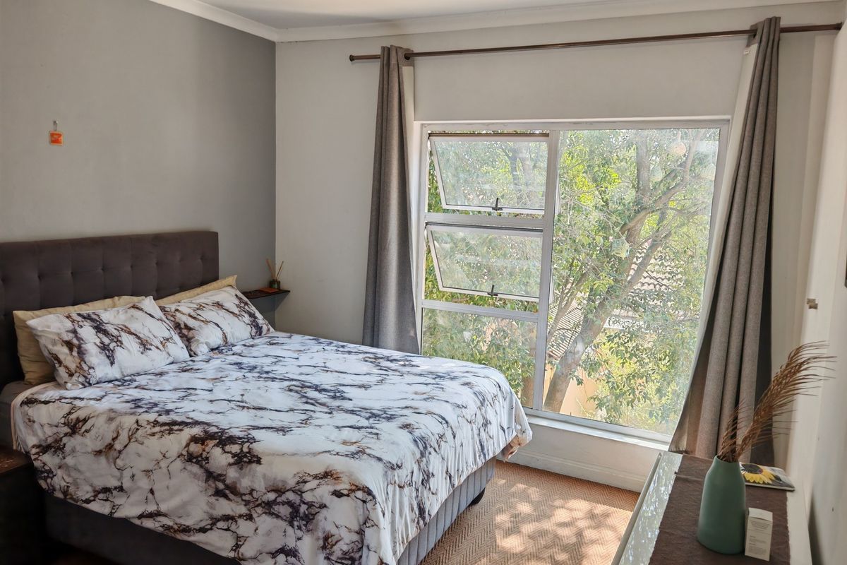 A well-lit bedroom featuring a large window with garden views, neutral wall finishes, and classic coving detail.