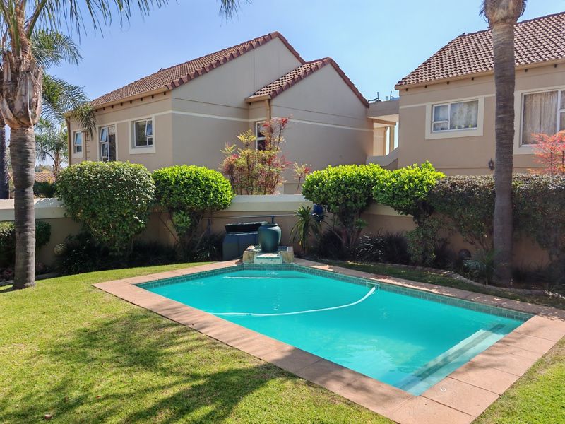 A well-maintained private swimming pool set within a landscaped garden, featuring a tiled coping and surrounding boundary wall in a townhouse complex.