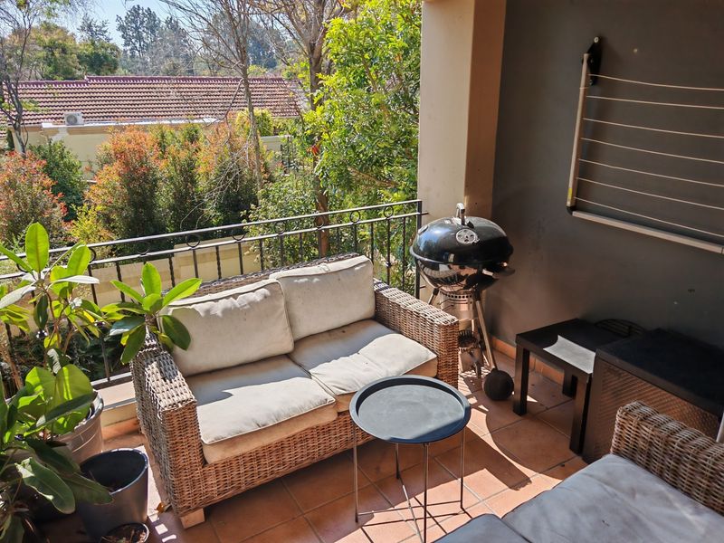 A covered balcony featuring tiled flooring, a wrought iron railing, and a wall-mounted drying rack, overlooking a leafy residential garden area.