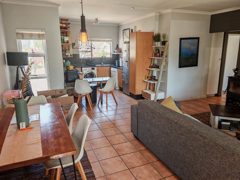 Open-plan living and kitchen area featuring tiled flooring, built-in cabinetry, and a cozy wood-burning fireplace, creating a functional and connected living space.