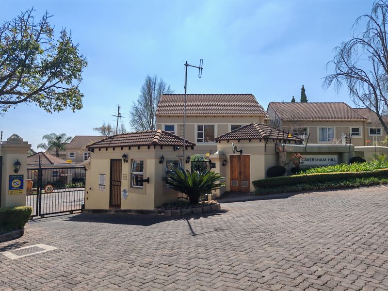 The entrance to Caversham Hill townhouse complex featuring a secure guard house, paved driveway, and perimeter electric fencing.