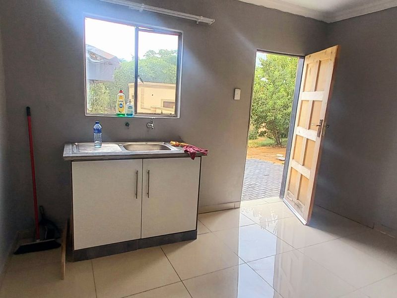 A compact kitchen area featuring tiled flooring, a single stainless steel sink with base cabinetry, and direct access to the exterior.
