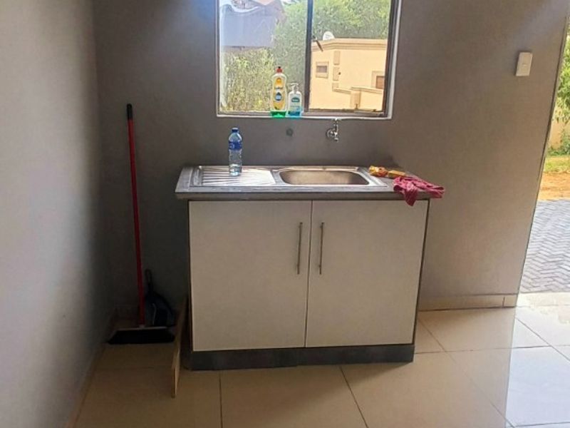 A compact kitchen area featuring a single stainless steel sink unit with base cabinetry and neutral tiled flooring.