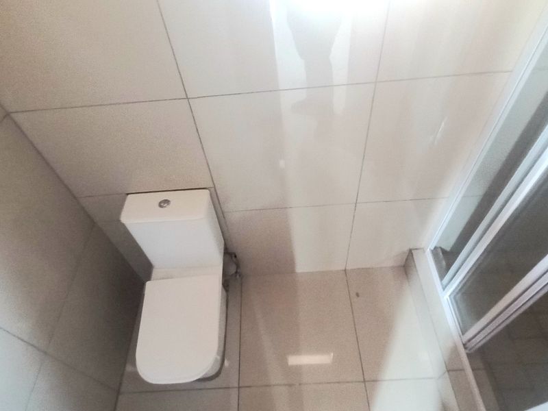 A compact bathroom featuring a modern toilet and a glass-enclosed shower, finished with neutral ceramic wall and floor tiles.