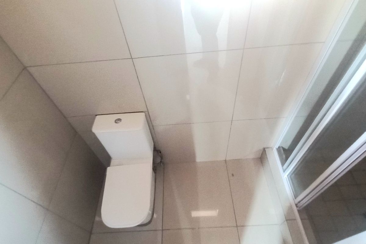 A compact bathroom featuring a modern toilet and a glass-enclosed shower, finished with neutral ceramic wall and floor tiles.