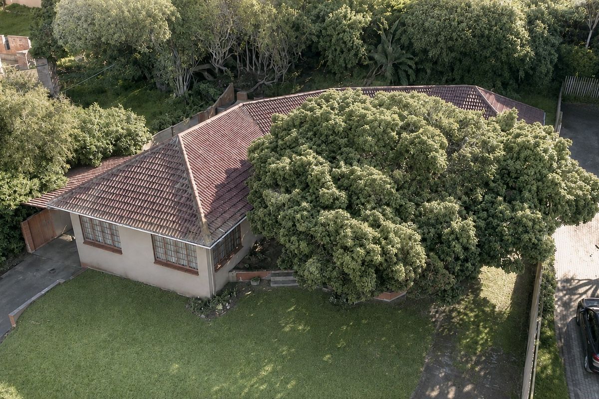 Aerial view of a residential property featuring a tiled roof, established garden, and driveway access.