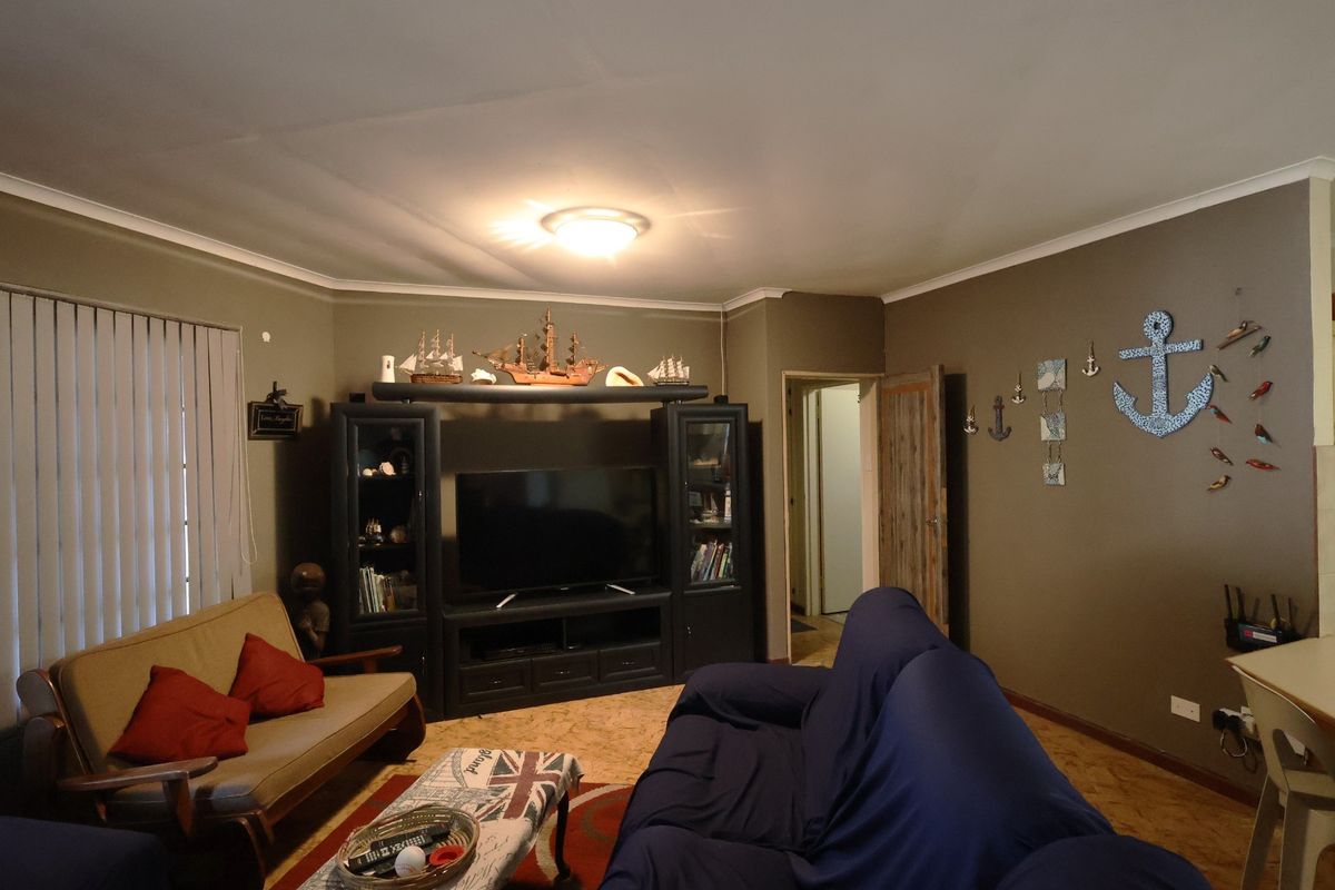 A living room featuring cork flooring, cove cornicing, and vertical blinds, providing a functional space with neutral wall tones.