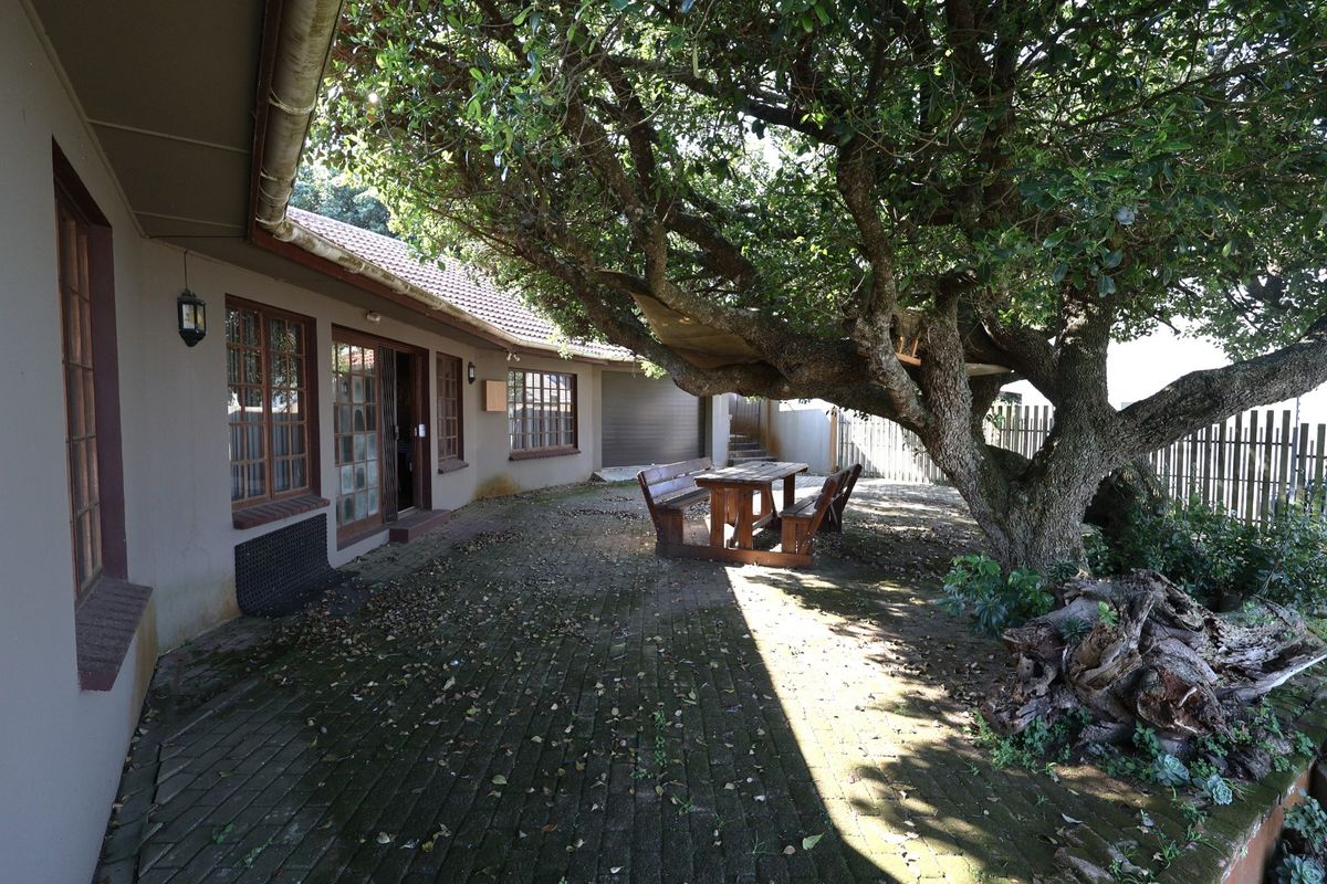 A rear exterior view featuring a paved patio area, mature tree, and direct access to the home through sliding glass doors.