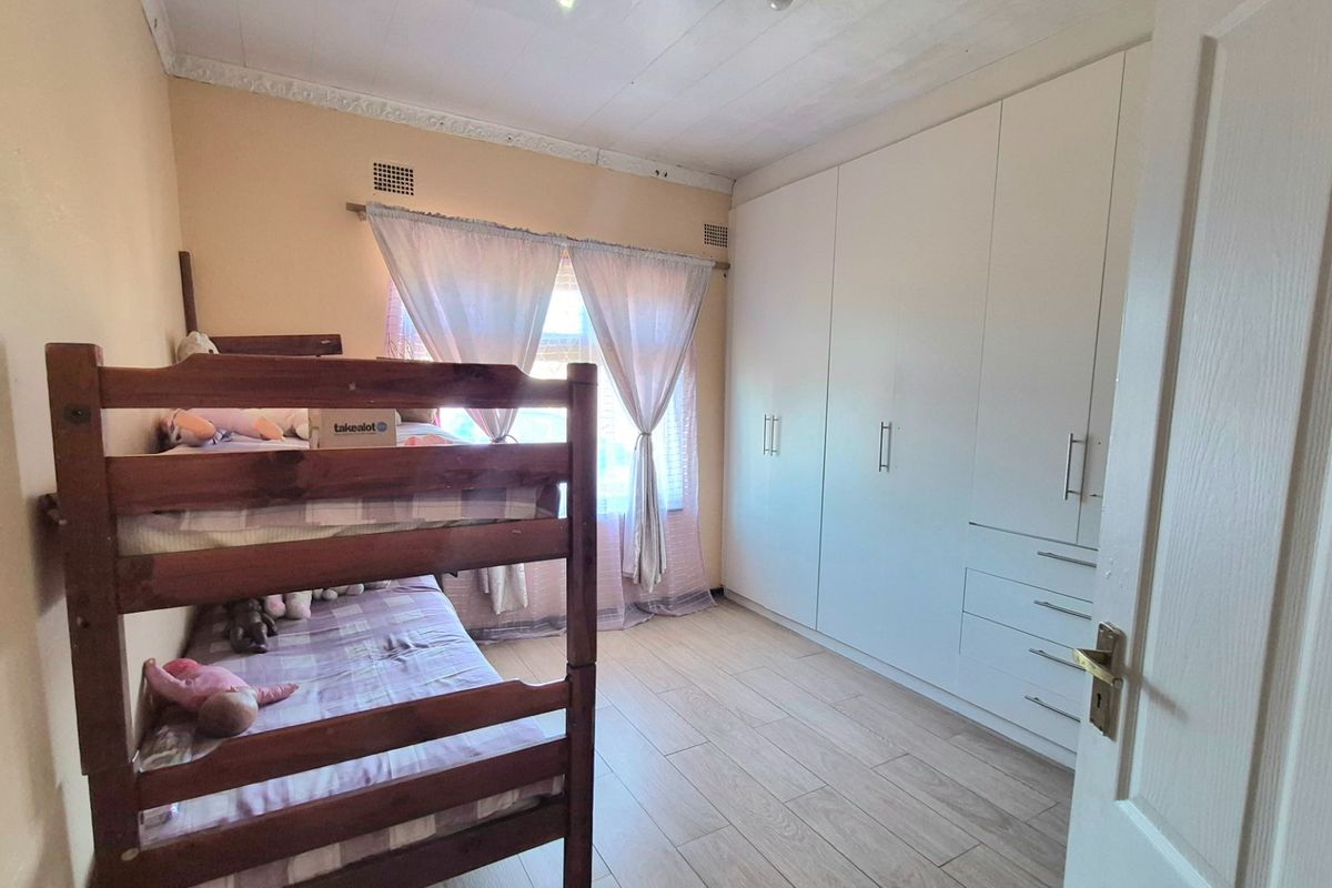 A bedroom featuring light-toned tiled flooring, built-in white cupboards, and a ceiling with decorative cornice detailing.