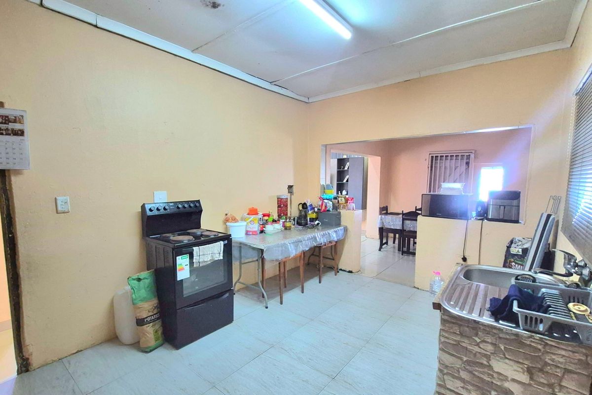 A functional kitchen area featuring tiled flooring, a freestanding stove, and a stainless steel sink, with an open-plan layout connecting to the dining space.