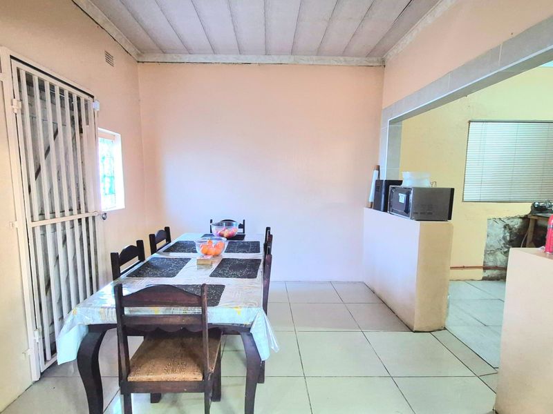 Open plan dining area featuring tiled flooring and a security gate, connecting to an adjacent kitchen space with a partial partition wall.