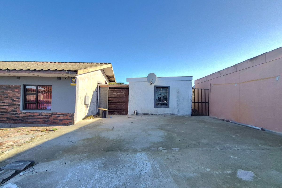 Rear exterior view of the property featuring a concrete driveway, security gate, and brick and rendered wall finishes.