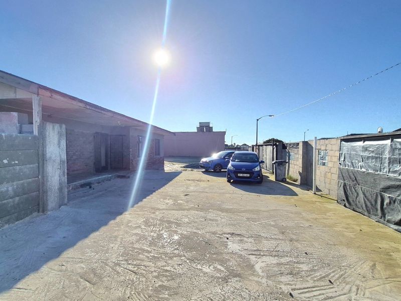 Rear exterior area featuring a concrete driveway, enclosed by precast concrete boundary walls and showing unfinished brickwork on the main structure.