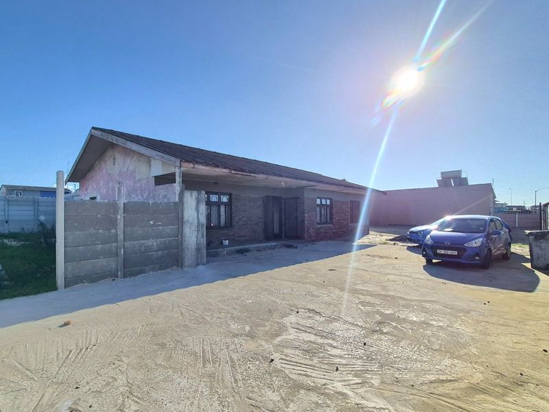 Front exterior view of a single-story house featuring a brick facade, tiled roof, and a large concrete driveway enclosed by precast boundary walls.