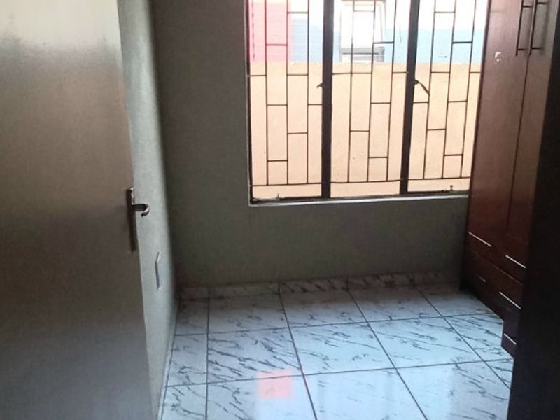 A compact bedroom featuring tiled flooring, a built-in wardrobe, and security bars on the window.