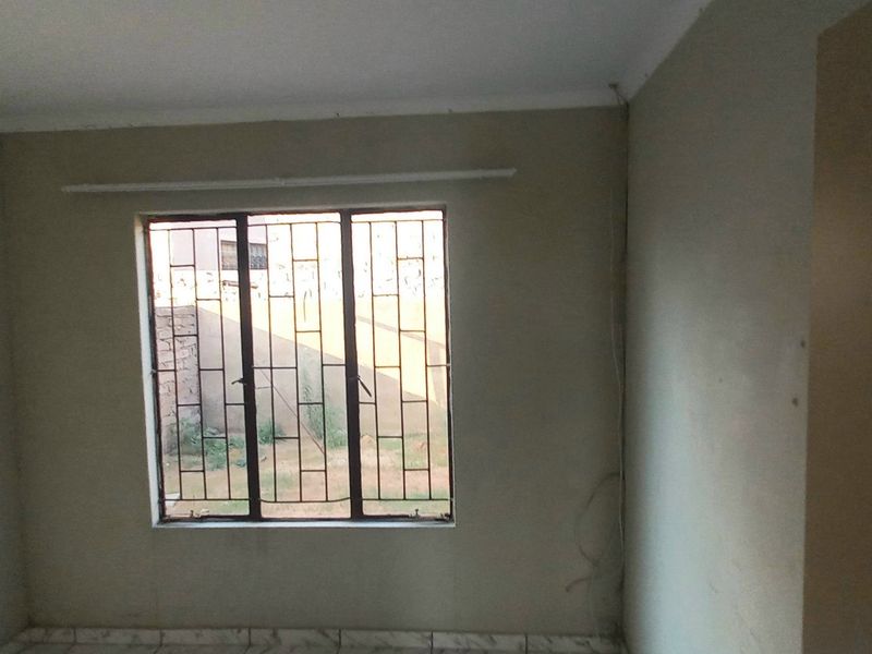 An empty bedroom featuring tiled flooring, security bars on the window, and coving. The room requires minor cosmetic updates and paint.