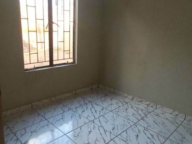 An empty bedroom featuring tiled flooring, neutral walls, and a window fitted with security bars.