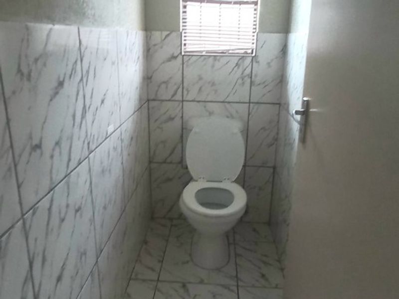 A compact guest bathroom featuring marble-effect wall and floor tiling and a standard toilet.