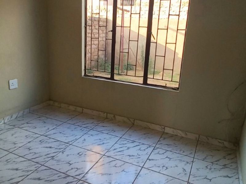 An empty bedroom featuring tiled flooring and a window fitted with security bars, offering a neutral space ready for personalization.