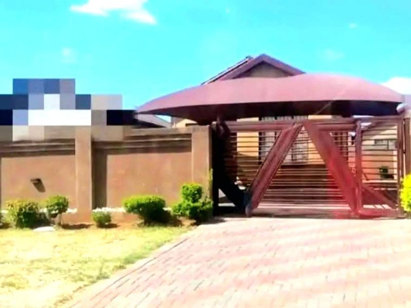 Front exterior view of the property featuring a paved driveway, secure perimeter wall, and a gated entrance with a covered carport.