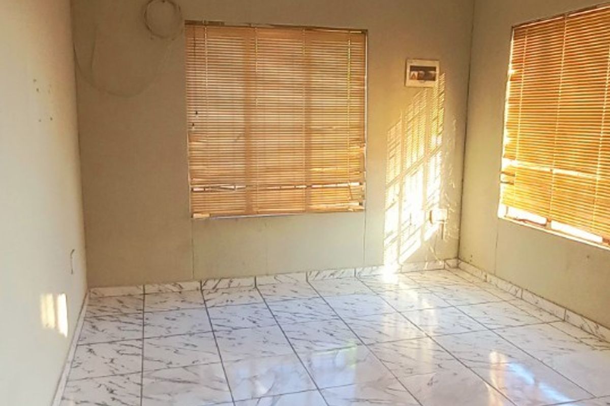 An empty living room featuring marble-look ceramic floor tiles, venetian blinds, and a neutral wall finish, ready for personalization.