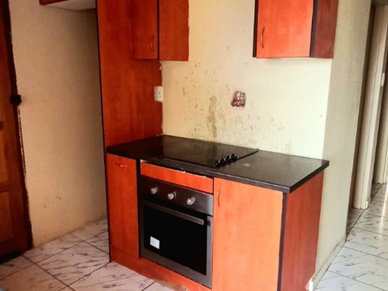 A compact kitchen area featuring built-in cabinetry, an integrated oven and hob, and tiled flooring, currently requiring cosmetic updates and wall repairs.