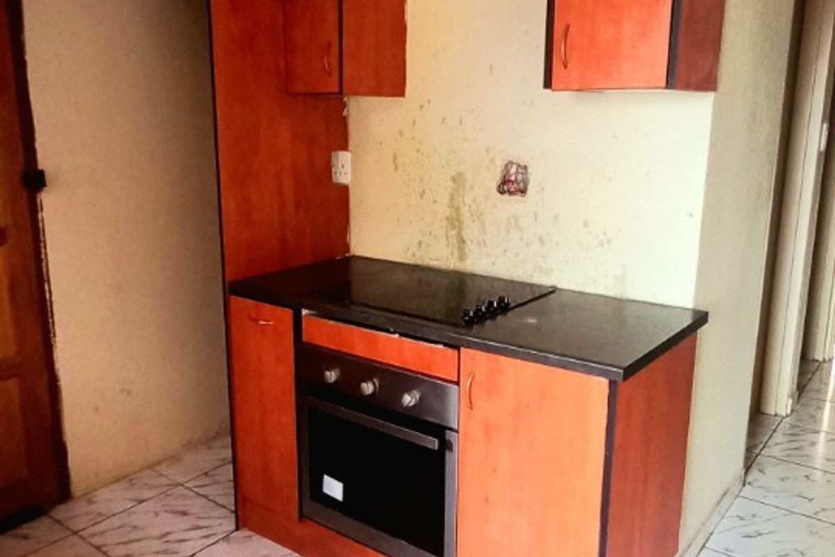 A compact kitchen area featuring built-in cabinetry, an integrated oven and hob, and tiled flooring, currently requiring cosmetic updates and wall repairs.