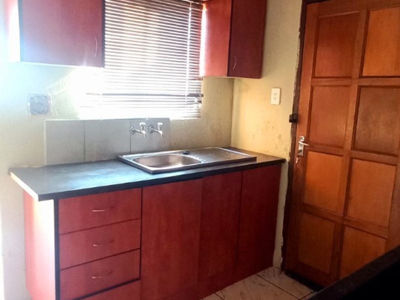 A functional kitchen area featuring dark wood-look cabinetry, a stainless steel sink, and tiled flooring, requiring cosmetic updates to modernize the space.