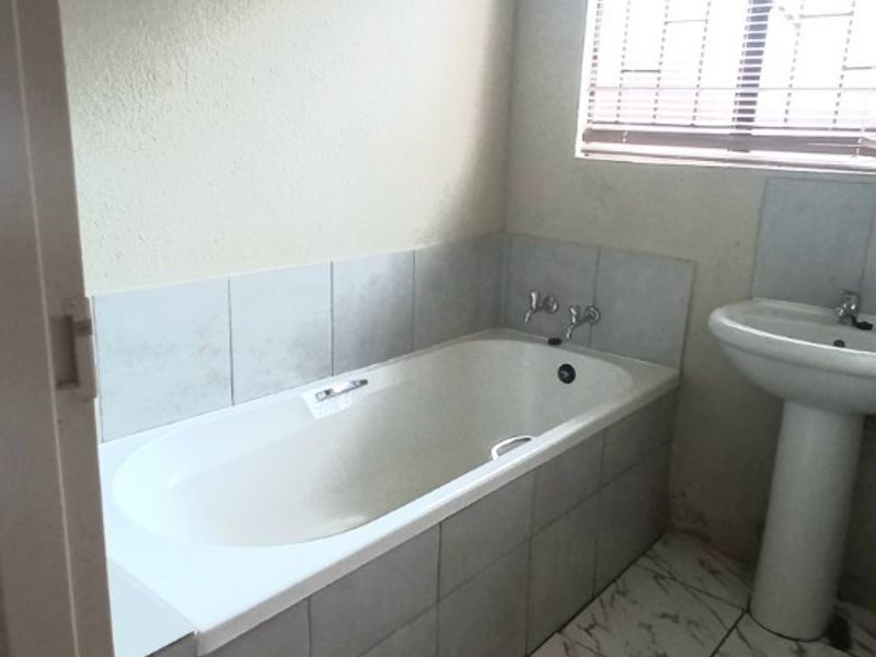 A functional bathroom featuring a built-in bathtub, pedestal basin, and marble-look tiled flooring with neutral wall finishes.