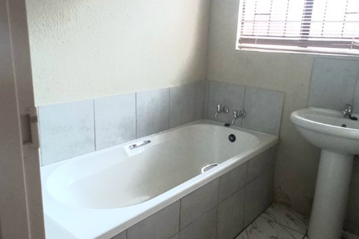 A functional bathroom featuring a built-in bathtub, pedestal basin, and marble-look tiled flooring with neutral wall finishes.