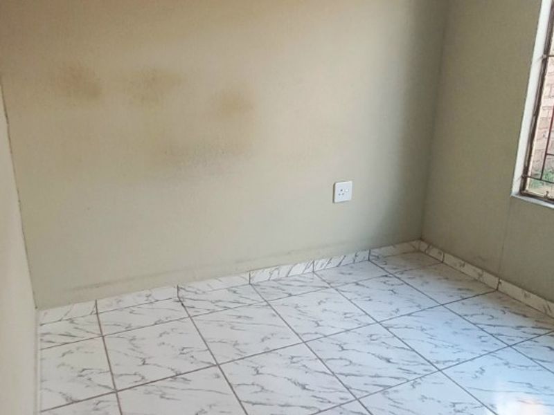 An empty bedroom featuring white marble-effect tiled flooring and neutral wall paint, requiring minor cosmetic attention to address visible wall staining.