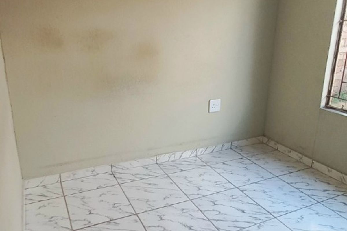 An empty bedroom featuring white marble-effect tiled flooring and neutral wall paint, requiring minor cosmetic attention to address visible wall staining.