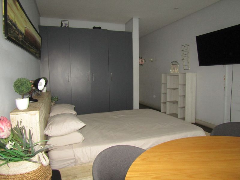 A bedroom featuring a large built-in wardrobe and recessed ceiling lighting, providing functional storage and a neutral living space.