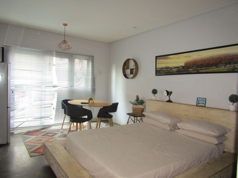 A well-lit bedroom featuring polished concrete flooring, modern pendant lighting, and large windows fitted with venetian blinds.
